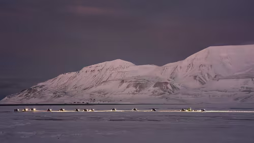 Hiorthhamn - Hike to Frozen Fjord Eine große Gruppe von Schneescootern fährt in das Adventdalen.