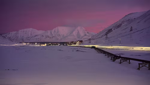 Rundgang Longyearbyen Blick vom „Vei 106“ auf Longyearbyen, links wo die schwarzen Schotterstreifen zu sehen sind, fließt im Sommer der „Longyearelva“. Rechts die oberirdischen Rohre...
